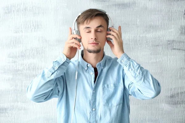 Jovem com fones de ouvido ouvindo música no fundo claro — Fotografia de Stock