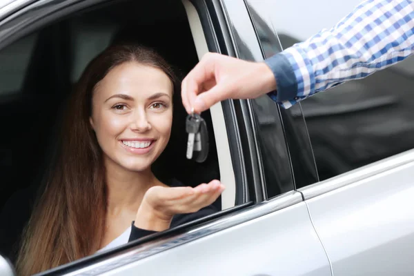 Jonge vrouw ontvangen sleutel zittend op de bestuurdersstoel van auto — Stockfoto