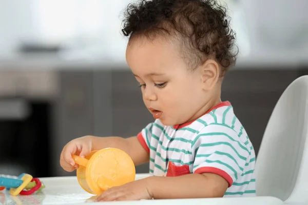 Schattige baby met flesje water zitten in de keuken — Stockfoto