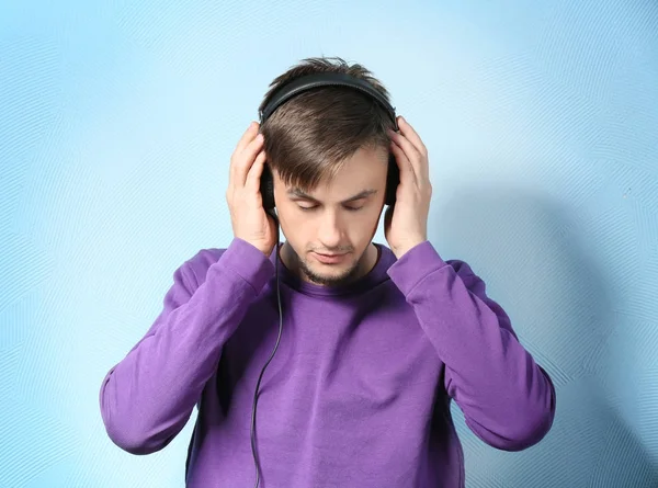 Young man with headphones listening to music on color background — Stock Photo, Image