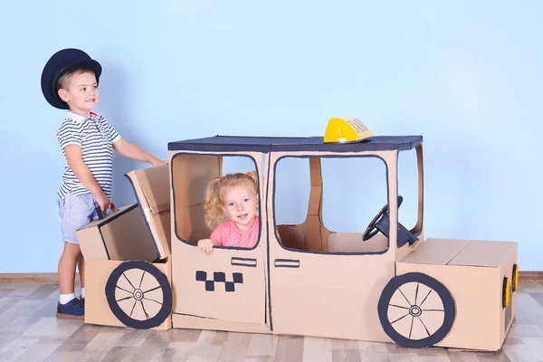 Little children playing with cardboard taxi in light room — Stock Photo, Image