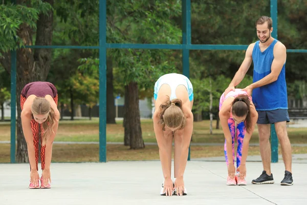 Hermosas mujeres jóvenes con entrenador haciendo ejercicio en el parque — Foto de Stock