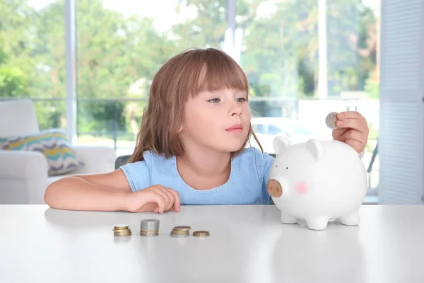 Cute Little Girl Putting Coin Piggy Bank Indoors — Stock Photo, Image