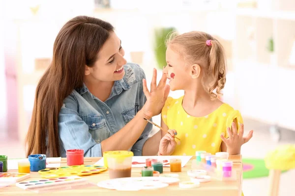 Nettes Mädchen mit Mutter beim Malen am Tisch drinnen — Stockfoto