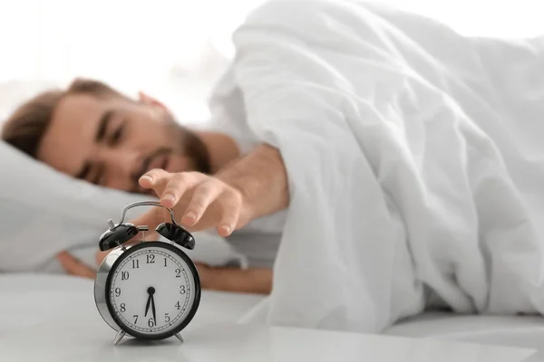 Young man switching off alarm clock signal while lying in bed at home — Stock Photo, Image