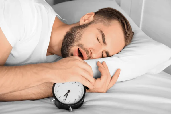 젊은 남자 집에서 침대에 누워 있는 동안 알람 시계 신호 끄기 — 스톡 사진