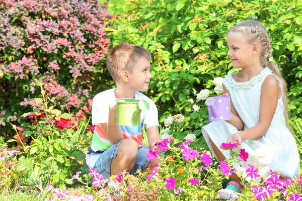 Niedliche kleine Kinder, die Blumen im Garten gießen — Stockfoto