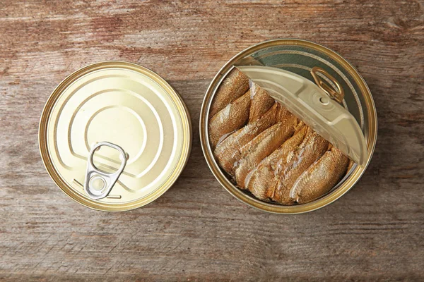 Open and closed tin cans with fish on wooden background