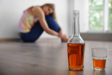 Arka planda kadın olan bir şişe ve bir bardak alkol.