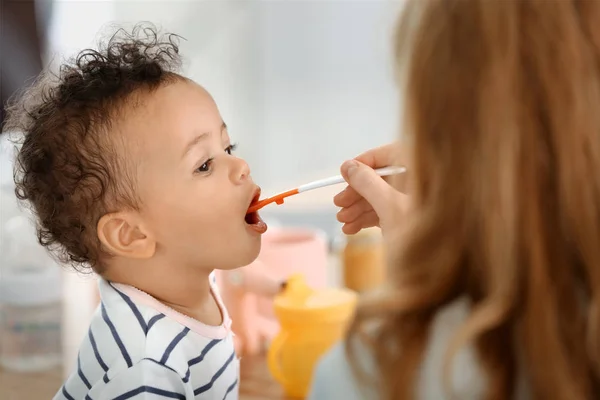 Mãe alimentando bebê com colher dentro de casa — Fotografia de Stock