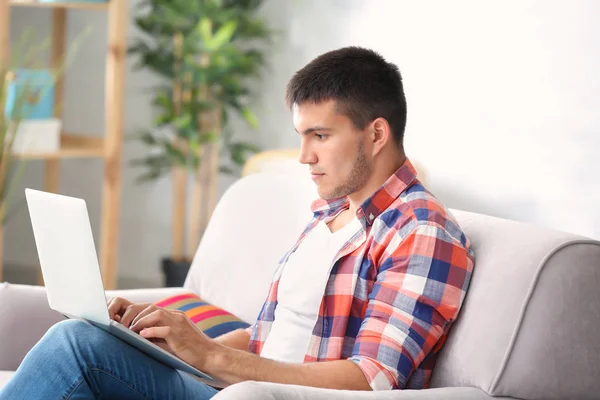 Ung man använder sin laptop medan du sitter på mysig soffa i rum — Stockfoto