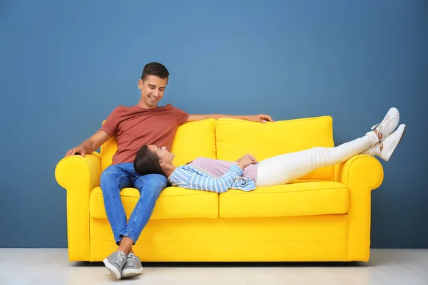 Молода пара на жовтому дивані біля кольорової стіни — стокове фото