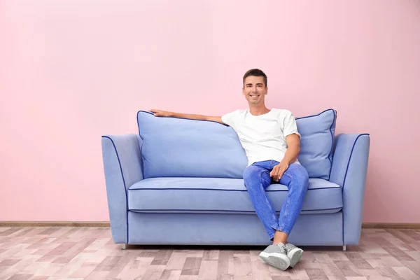 Hombre joven en sofá azul cerca de la pared de color — Foto de Stock