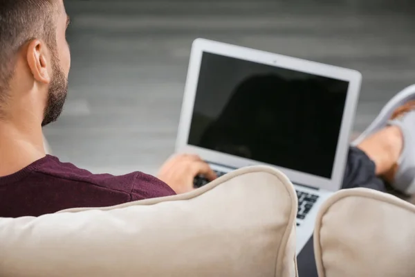 Young man with modern laptop on sofa at home — Stock Photo, Image