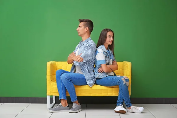 Jeune couple assis sur un canapé jaune près du mur de couleur — Photo