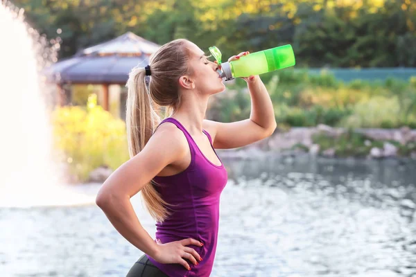 Sporty young woman drinking water on riverside — Stock Photo, Image