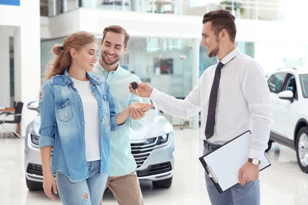 Venditore di auto dando la chiave per coppia in concessionaria — Foto Stock