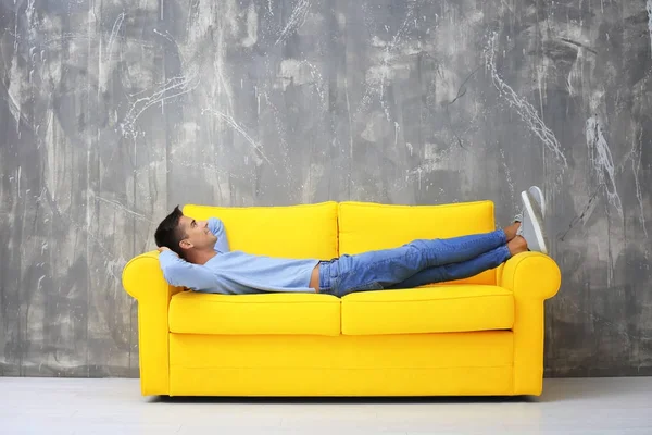 Молодий чоловік лежить на жовтому дивані біля сірої стіни — стокове фото