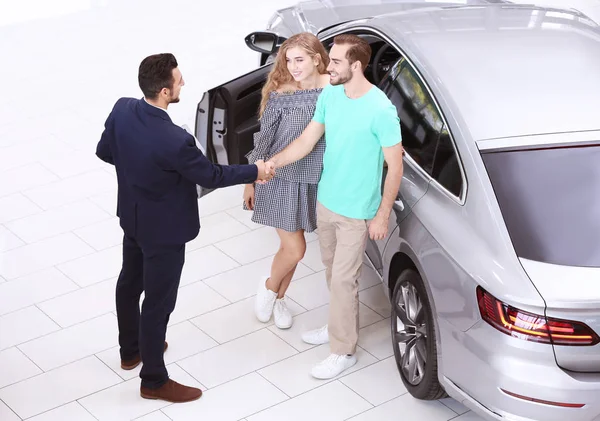 Car salesman and young couple in dealership — Stock Photo, Image