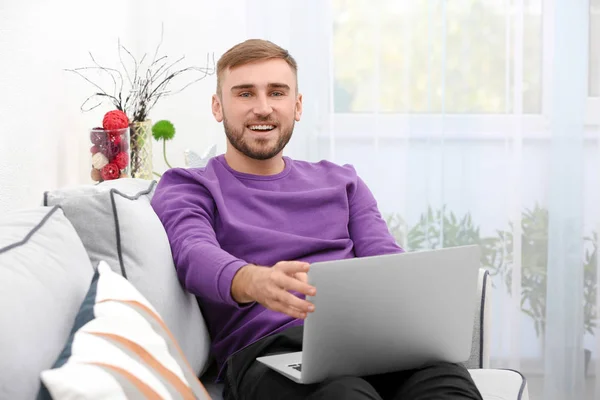 Hombre joven con portátil moderno en el sofá en casa — Foto de Stock