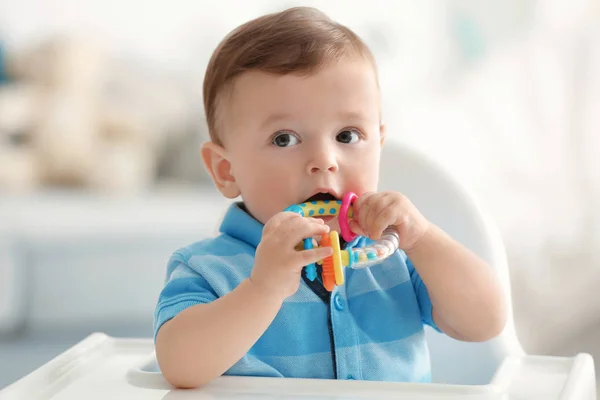 Cute baby z grzechotką siedzi na krześle w pomieszczeniu — Zdjęcie stockowe