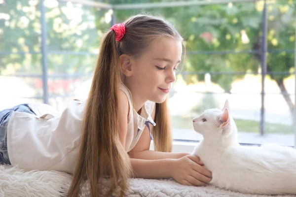 Kleine meisje en witte kat liggend op de vensterbank binnen — Stockfoto