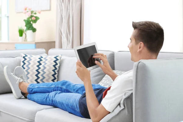 Hombre joven usando tableta en el sofá en casa — Foto de Stock