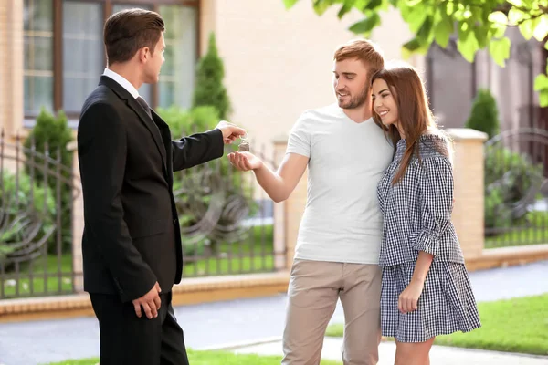 Onroerende goederenagent geven sleutel tot jonge paar in de buurt van huis — Stockfoto