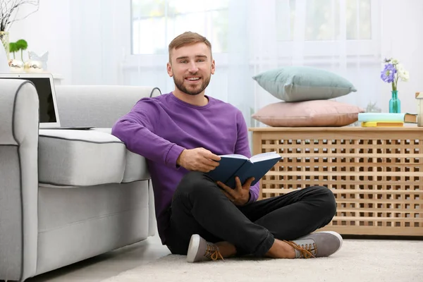 Молодий чоловік читає книгу на підлозі біля дивана вдома — стокове фото