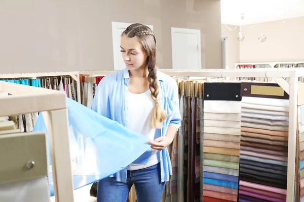 Młoda kobieta wybierając tkaniny na nowe zasłony w sklepie — Zdjęcie stockowe