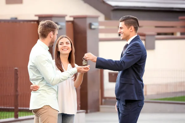 Immobilienmakler übergibt Schlüssel an junges Paar in der Nähe von Haus — Stockfoto