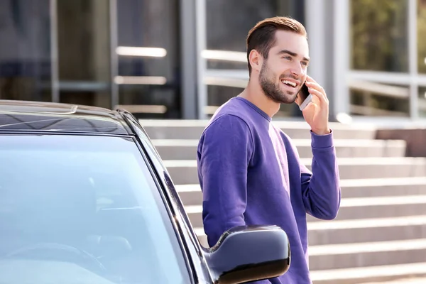 Handsome young man talking on mobile phone near car outdoors — Stock Photo, Image