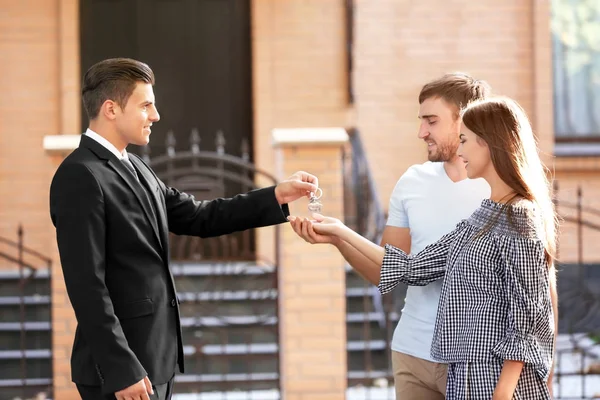 Immobilienmakler übergibt Schlüssel an junges Paar in der Nähe von Haus — Stockfoto