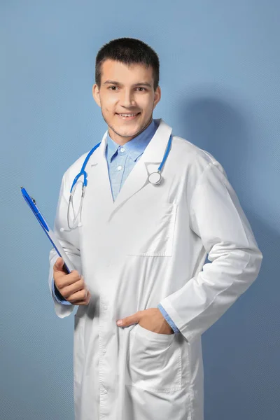 Young male doctor with clipboard against color background — Stock Photo, Image