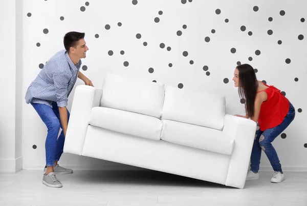 Молода пара носить диван біля білої стіни — стокове фото