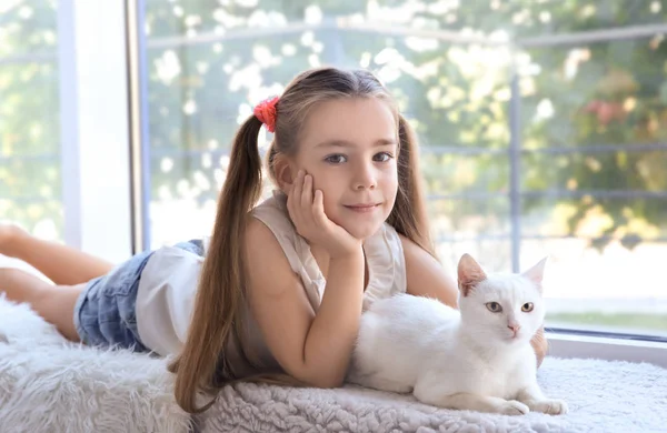 Kleine meisje en witte kat liggend op de vensterbank binnen — Stockfoto