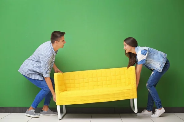 Pareja joven llevando sofá amarillo cerca de la pared de color — Foto de Stock