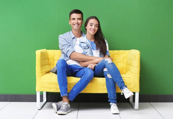 Giovane coppia seduta sul divano giallo vicino alla parete di colore — Foto Stock