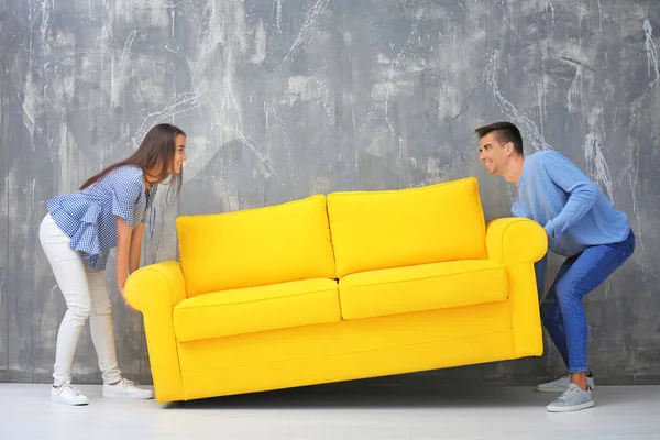 Молода пара носить жовтий диван біля сірої стіни — стокове фото