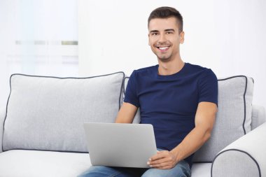 Evde kanepe üzerinde modern dizüstü bilgisayar ile genç adam