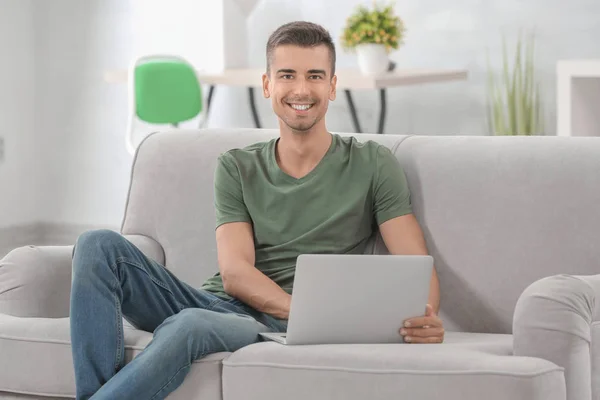 Молодой человек с современным ноутбуком на диване дома — стоковое фото
