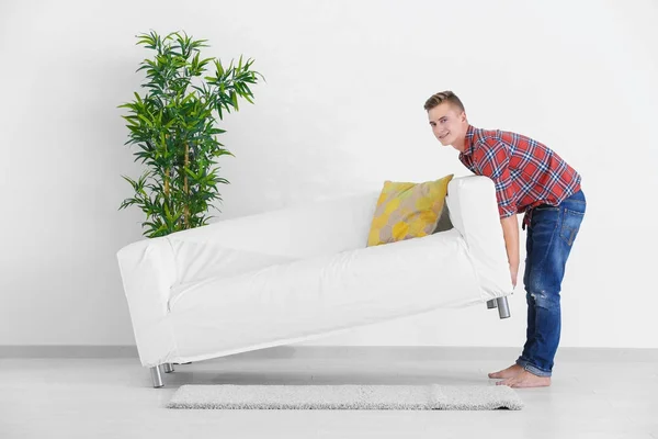 Молодий чоловік рухає диван в кімнаті в новому будинку — стокове фото