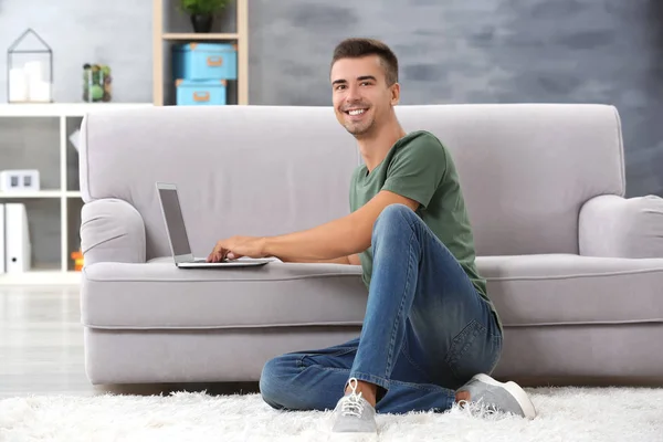 Young man with modern laptop near sofa at home — Stock Photo, Image