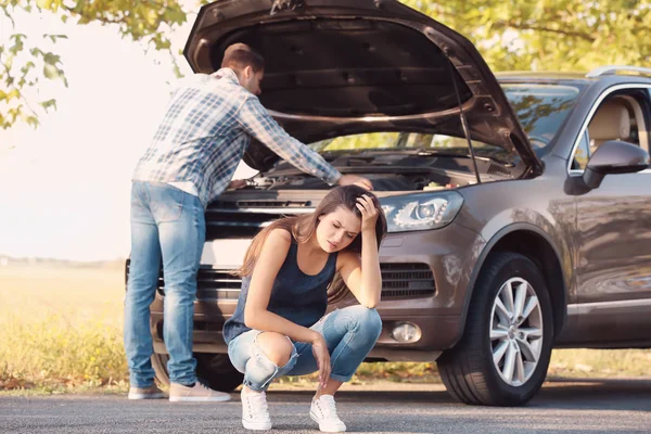 Mladá žena a muž s rozbité auto na pozadí — Stock fotografie