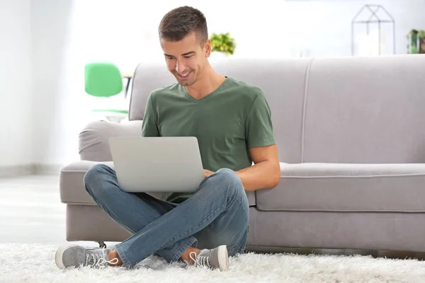 Giovane con computer portatile moderno vicino al divano a casa — Foto Stock