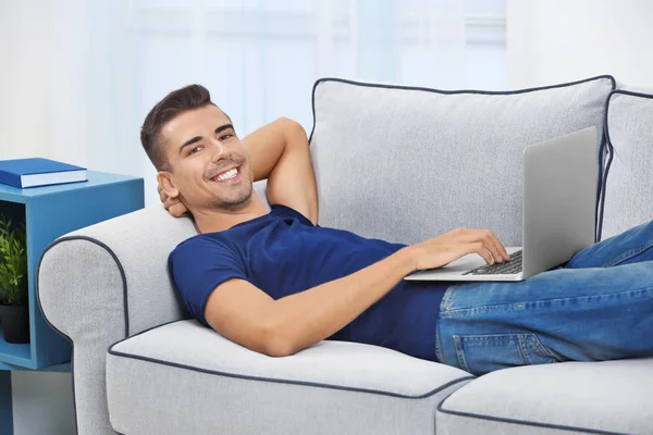 Hombre joven con portátil moderno en el sofá en casa —  Fotos de Stock