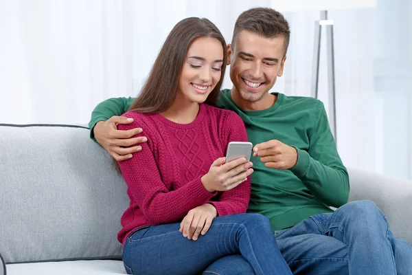 Casal jovem com telefone no sofá em casa — Fotografia de Stock