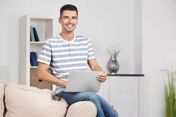 Молодой человек с современным ноутбуком на диване дома — стоковое фото