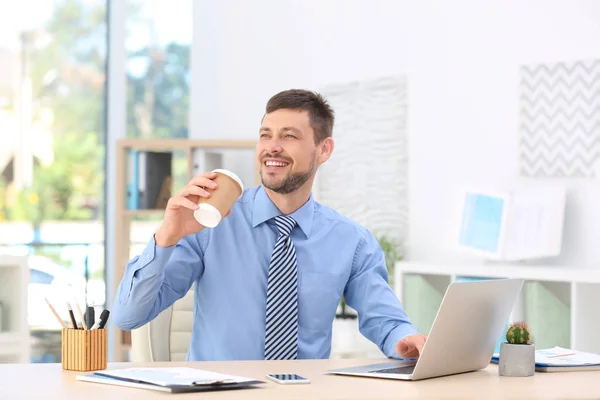 Hombre de negocios guapo bebiendo café mientras trabaja en la oficina — Foto de Stock