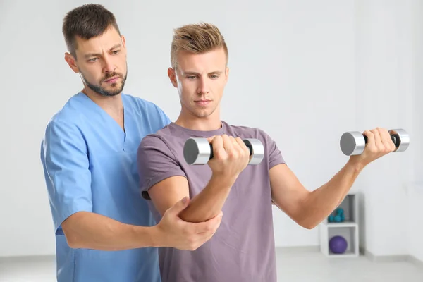 Fisioterapeuta que trabaja con un paciente masculino joven en la clínica — Foto de Stock